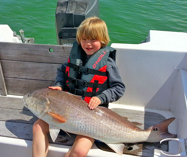 Child wearing PFD holding redfish fishing boat Pensacola Beach, Pensacola, Florida