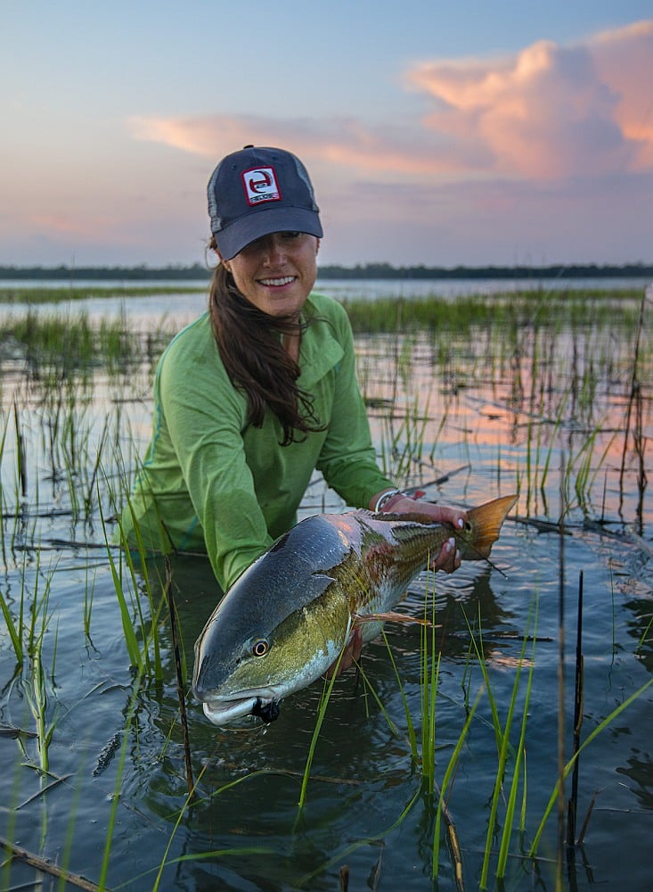 Lady angler releasing big redfish caught saltwater fishing in South Carolina Lowcountry marsh