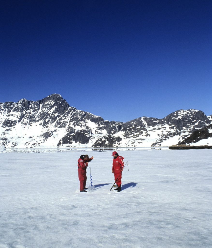 Drilling fishing holes through Greenland sea ice