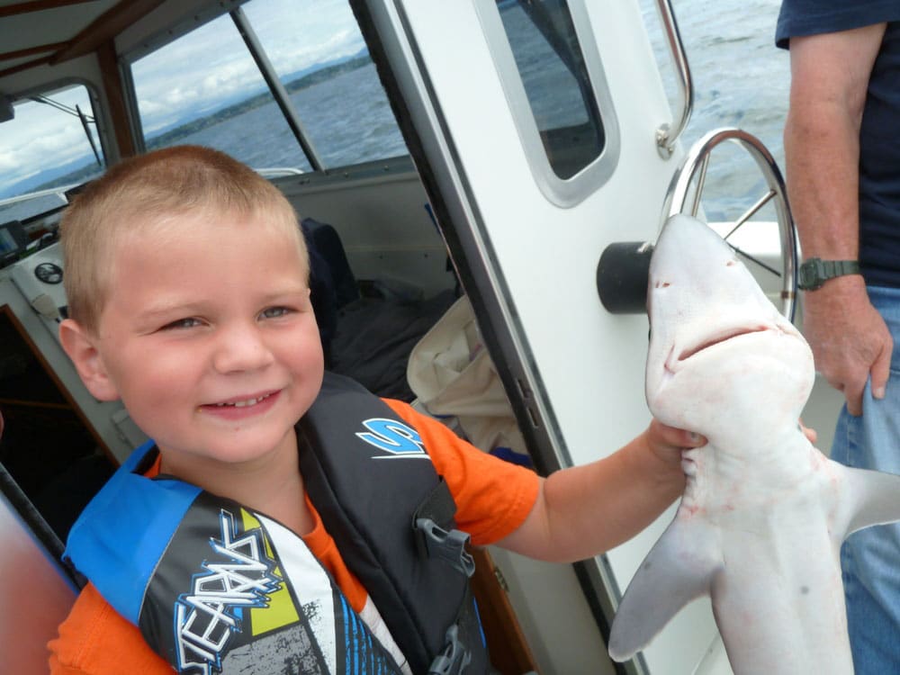 Child fisherman wearing life jacket holding shark fishing boat Point Migley, Lummi Island, Washington