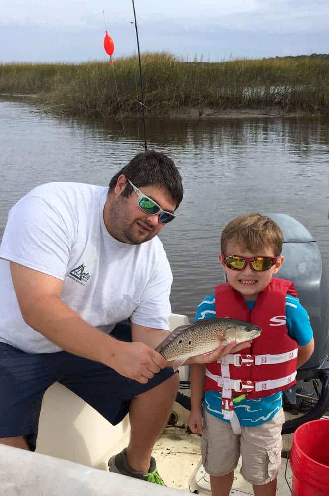 Boy wearing life jacket with father redfishing Wando River, South Carolina