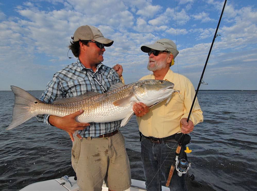 Bull red drum held by angler and fisherman with spinning reel and fishing rod