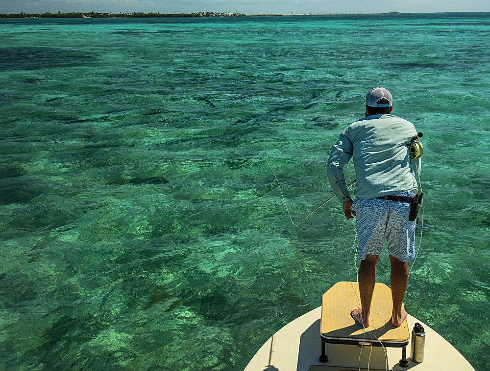 Angler casting toward school of tarpon from saltwater flats skiff fishing boat