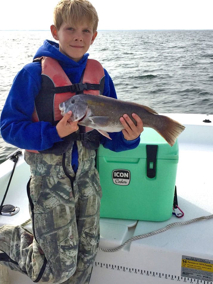 Boy wearing life jacket holding black seabass Chesapeake Bay, Poquoson, Virginia