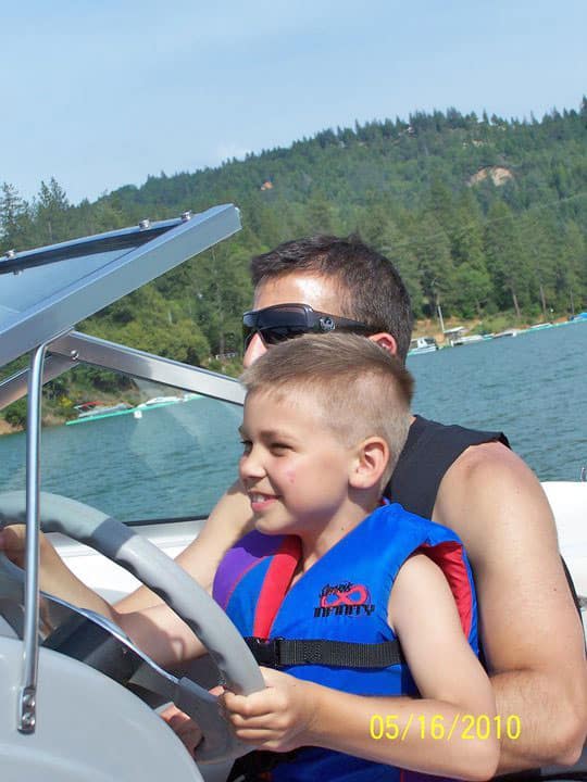 Boy wearing life jacket with dad boating Rollins Lake