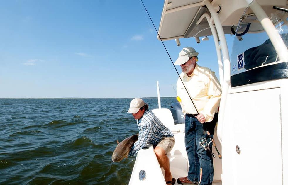 Angler releasing a redfish into North Carolina's Pamlico Sound fisherman holding spinning reel combo