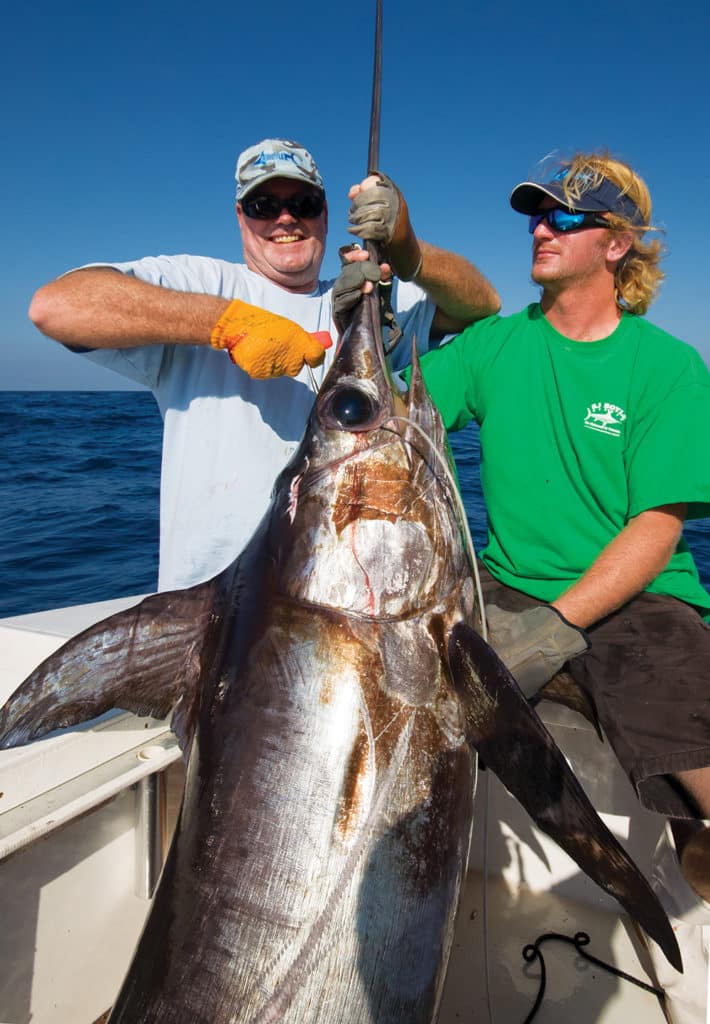 Two fishermen holding a swordfish caught deep sea fishing near the bottom.