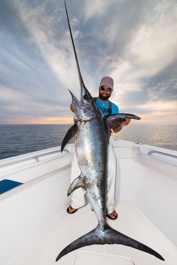Fisherman holding a swordfish caught on rod and reel in a fishing boat
