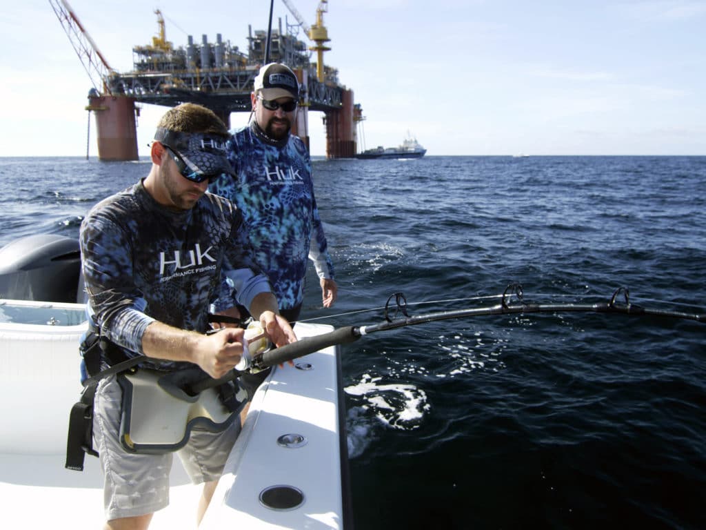 A fisherman fighting a yellowfin tuna on stand-up fishing gear in the Gulf of Mexico around an oil rig