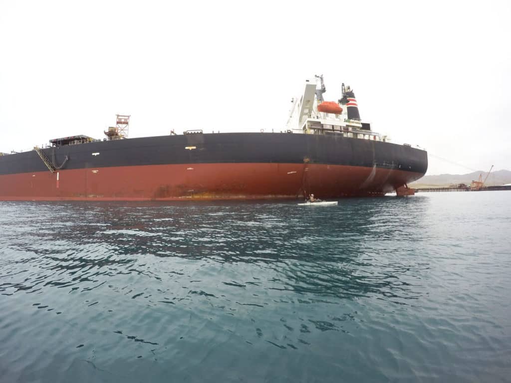 A kayak angler fishes near a huge tanker.