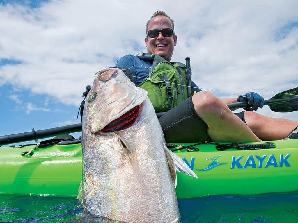 Kayak angler holding amberjack (AJ) fish next to a fishing kayak