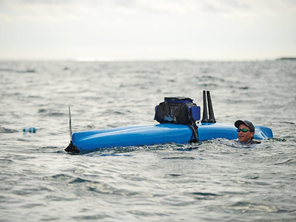 Angler in ocean next to fishing kayak flipped over