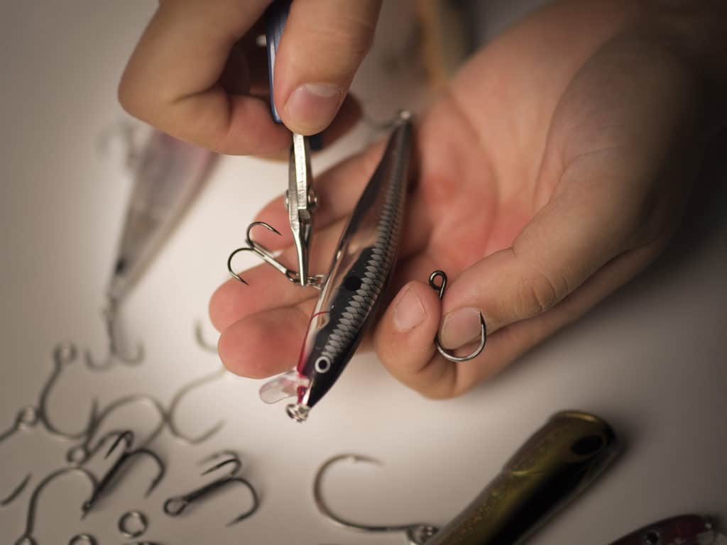 Fisherman using fishing pliers to switch a treble hook to a single hook on a saltwater fishing lure