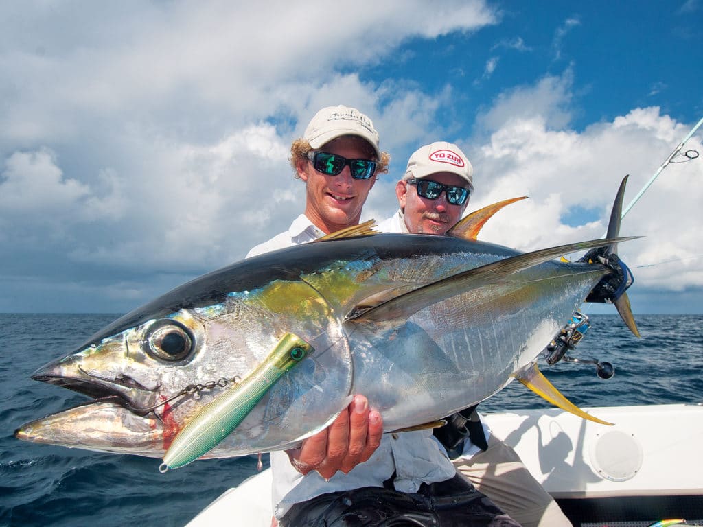 Angler holding a yellowfin tuna caught fishing with a popper fishing lure and an aftermarket single hook