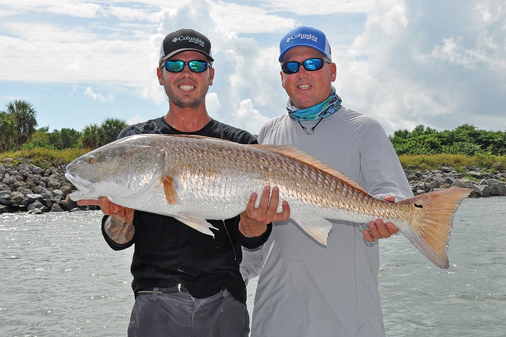 Two anglers holding a bull redfish caught fishing rock jetties