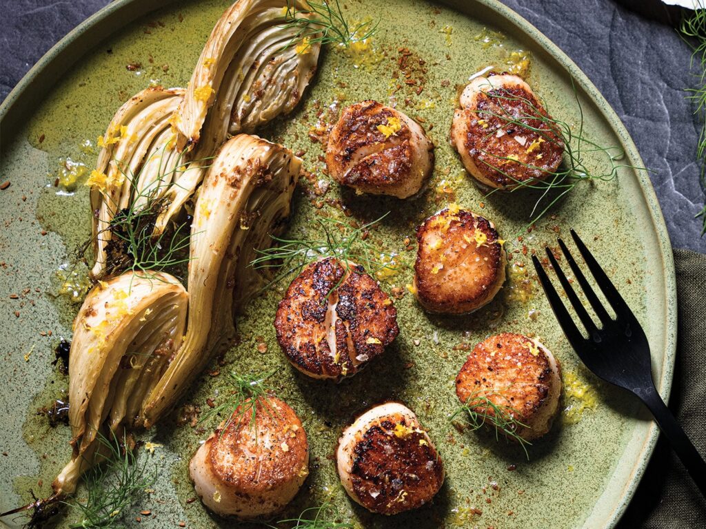 A plate of pan-seared scallops next to seared fennel