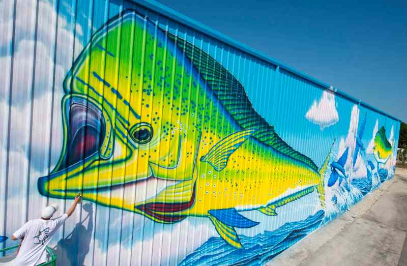 Artist David Dunleavy puts finishing touches on a huge mural entitled "Dolphin Rodeo" Friday, Oct. 30, 2016, at Tavernier Creek Marina in Islamorada, Fla. The 252-foot-wide by 33-foot-high artwork features two dolphin, also known as mahi-mahi, that are popular ocean gamefish caught off the Florida Keys and other regions of the world. The New Jersey artist worked seven to eight hours each day for 23 days to paint his 62nd larger-than-life SeaLife Mural. FOR EDITORIAL USE ONLY (Andy Newman/Florida Keys News Bureau/HO)